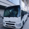 White Luxury Coach Bus – SSM Chauffeurs White luxury coach bus parked beside a modern building